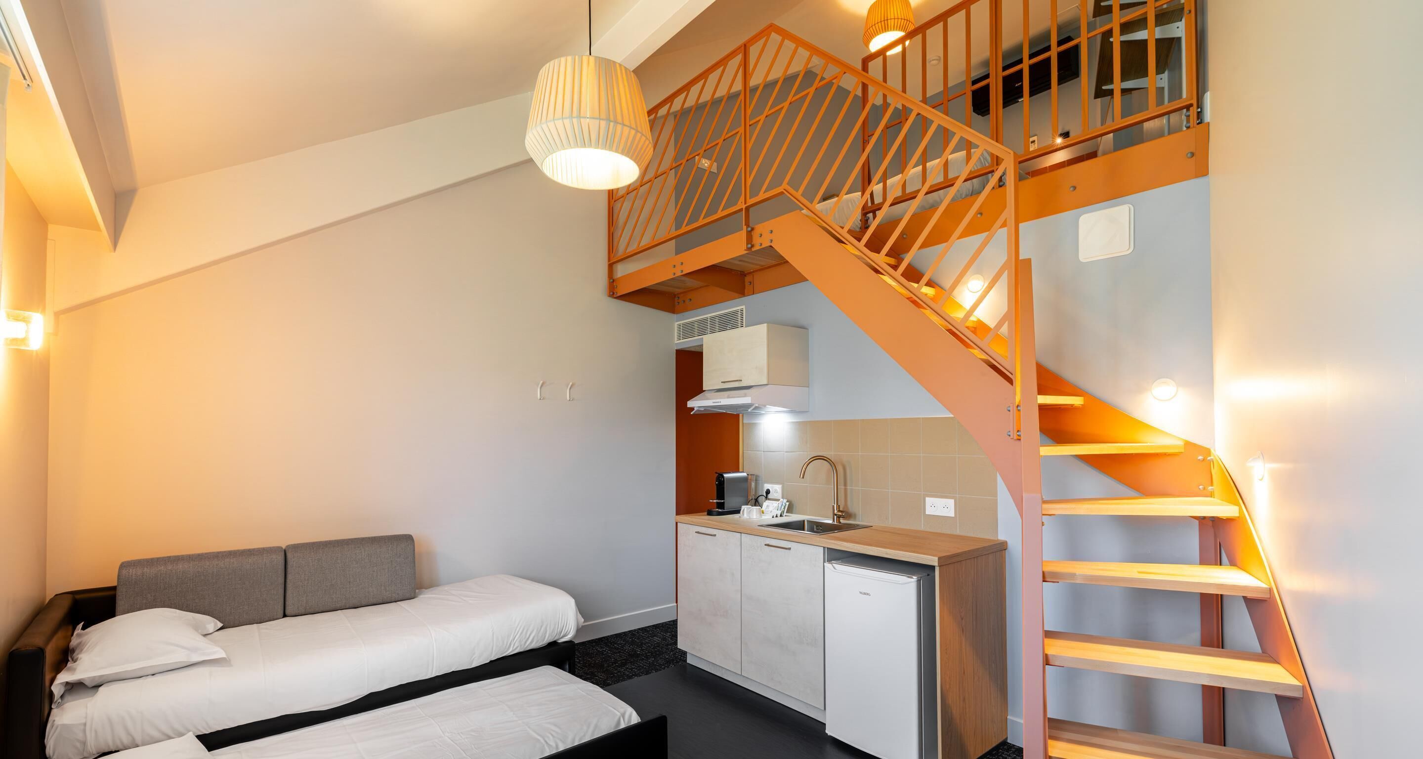 A bedroom with a bed, a kitchenette, and a staircase.