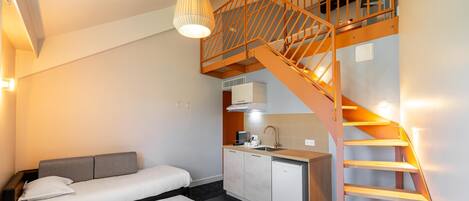 Un dormitorio con cama, kitchenette y escalera.
