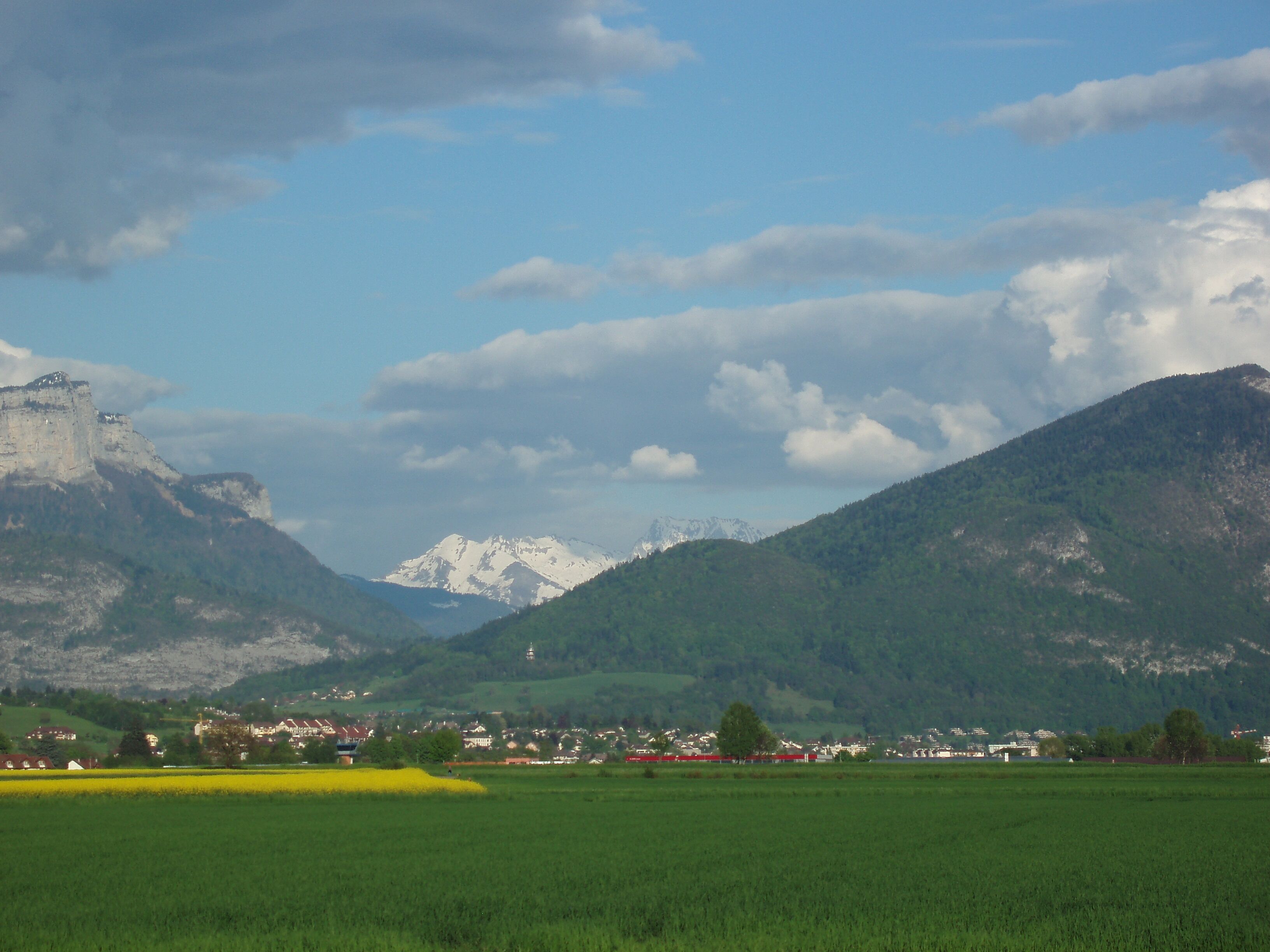 A mountainous landscape with a castle, green fields, and a small town.