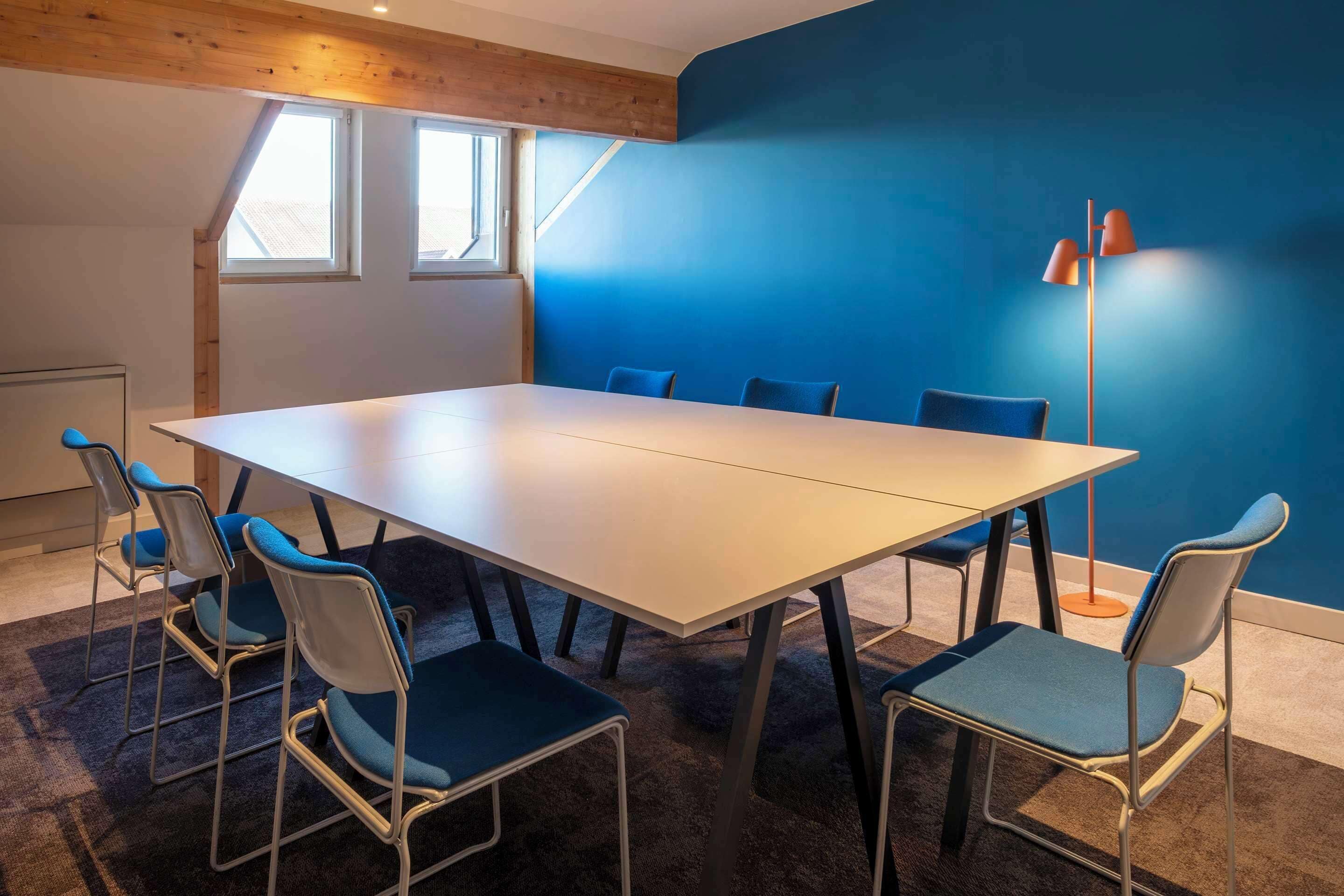 A conference room with a large table and six chairs, a floor lamp, and a blue wall.