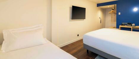 Habitación de hotel con dos camas, un televisor de pantalla plana montado en la pared, una viga de techo de madera, y un escritorio pequeño con un espejo y una cafetera.