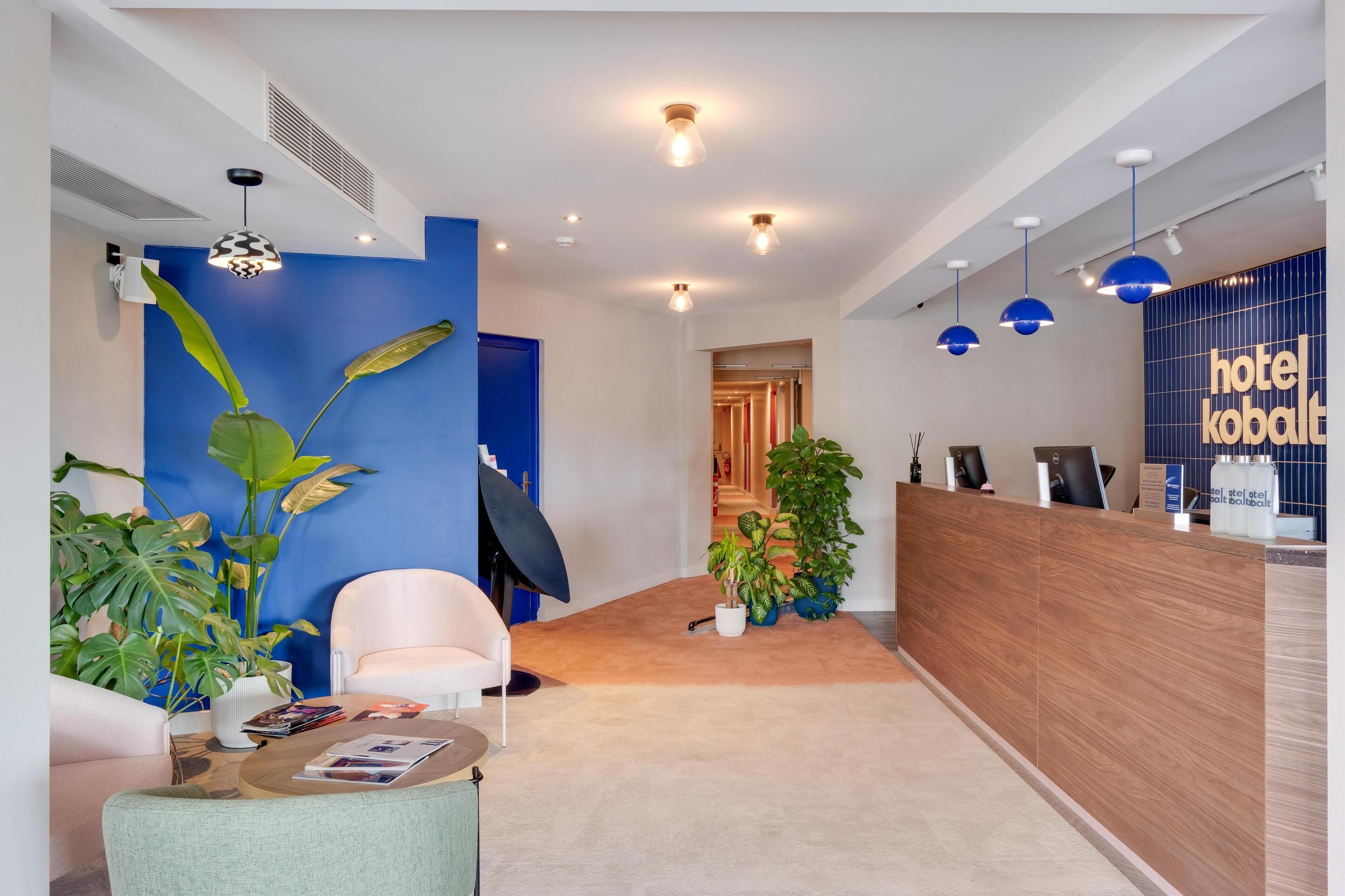 Een moderne hotel lobby met een receptiebalie, een zithoek en decoratieve planten.