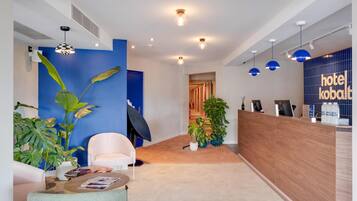 Een moderne hotel lobby met een receptiebalie, een zithoek en decoratieve planten.