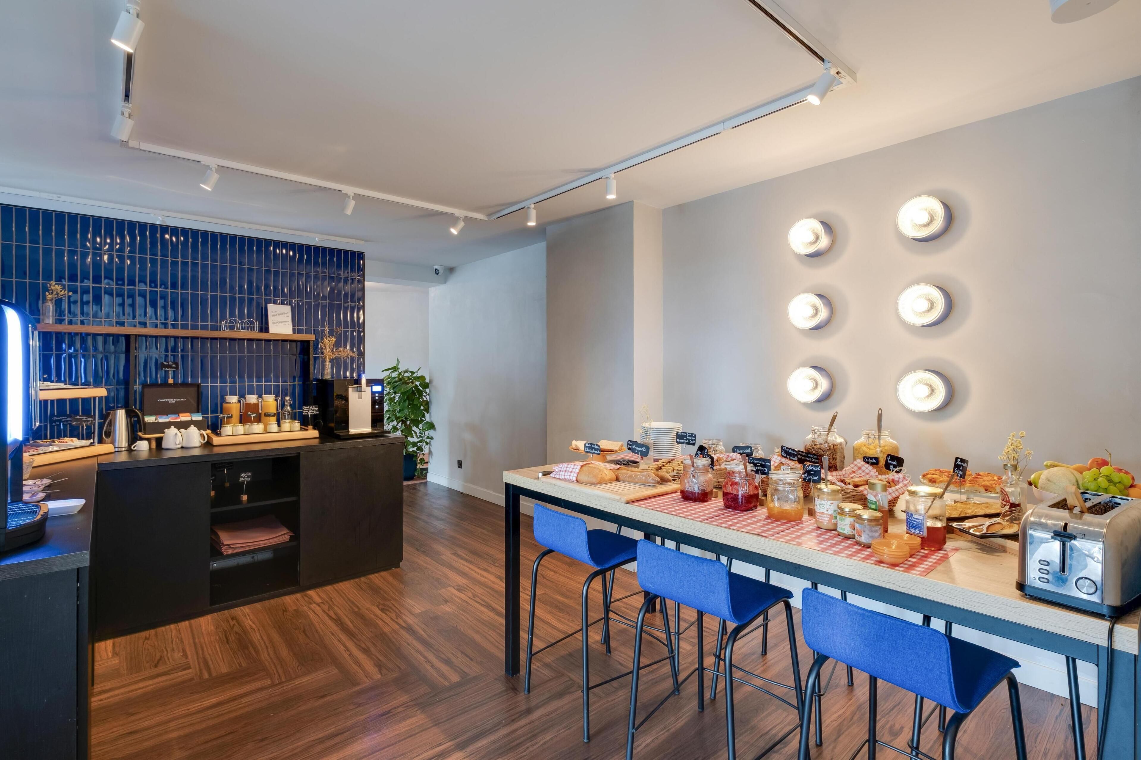 A modern kitchen with a wooden countertop, blue bar stools, and a breakfast bar with various food items and a coffee machine.