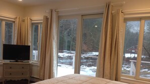A bedroom with a large bed, a television on a dresser, and a view of a snowy outdoor area through the windows.