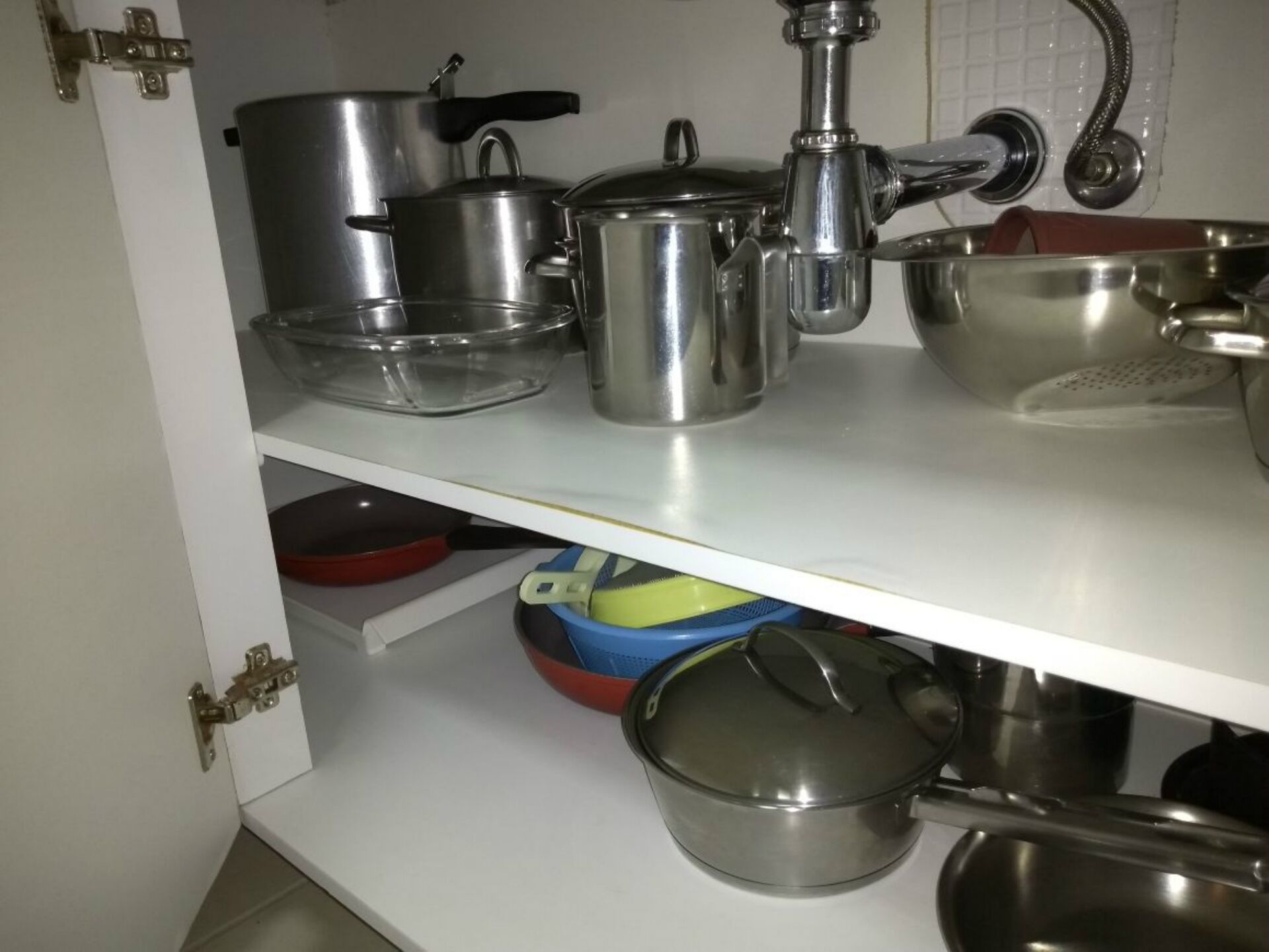 A kitchen with stainless steel cookware, including pots, pans, and a kettle, on white shelves.