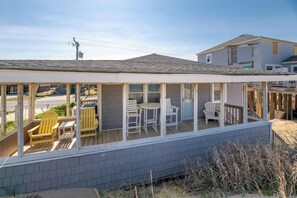 Une terrasse extérieure couverte, dotée de chaises et d’une table, une clôture en bois et une maison en arrière-plan.