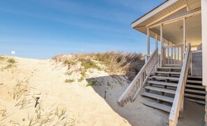 A beach house with a wooden staircase leading to a covered porch.