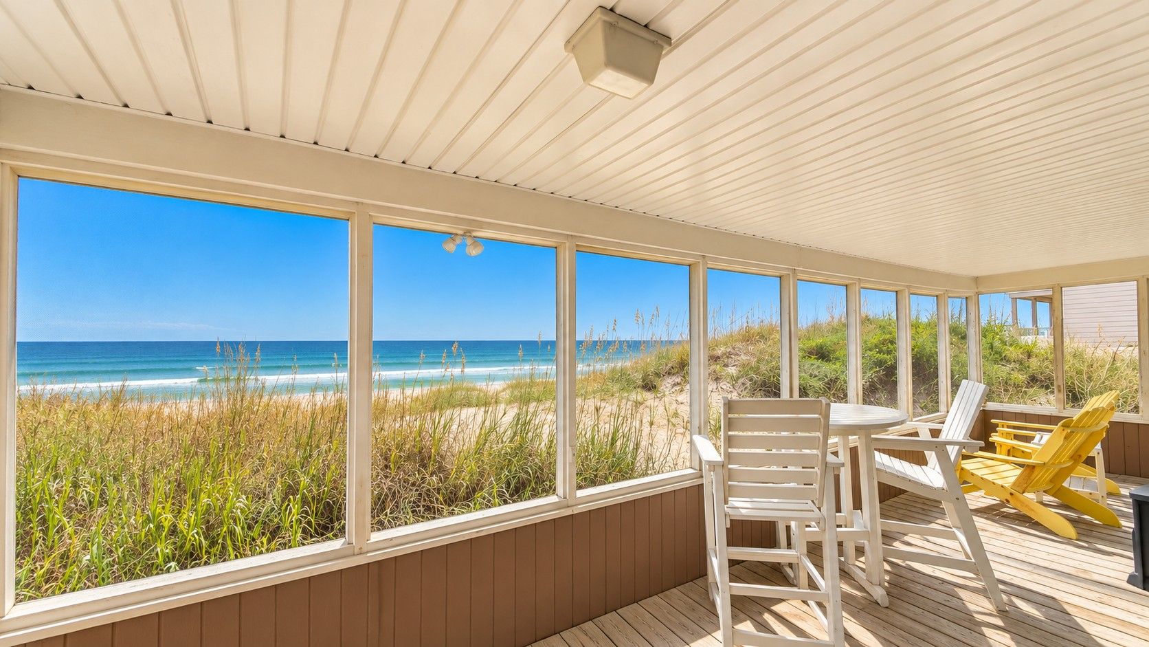 A covered outdoor area with a view of the beach, wooden deck, and seating.