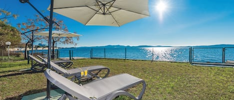 A grassy area with lounge chairs and umbrellas overlooking a body of water.