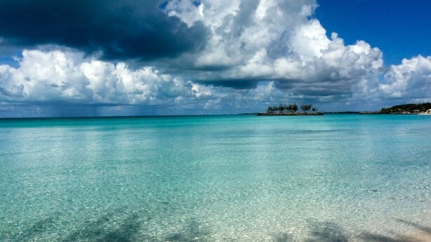 Una playa con aguas turquesas cristalinas y una gran formación de nubes en el cielo.