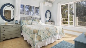 Un dormitorio con cama, cómoda, dos espejos redondos, mesita de noche y ventana con vistas a árboles.