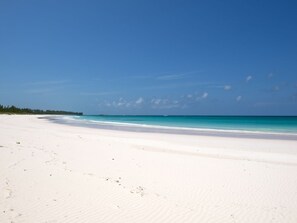 A wide, white sandy beach with clear turquoise water and a clear blue sky.
