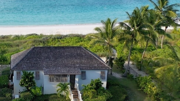 A coastal house with a paved driveway, surrounded by lush greenery and palm trees, overlooking a beach and turquoise waters. - Stunning Luxury Villa Directly On French Leave Beach (Governors Harbour)