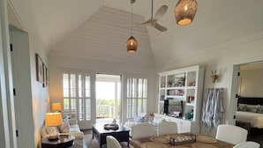 A spacious living room with a high ceiling, a dining area with a wooden table, white upholstered chairs, and a ceiling fan. - Stunning Luxury Villa Directly On French Leave Beach (Governors Harbour)
