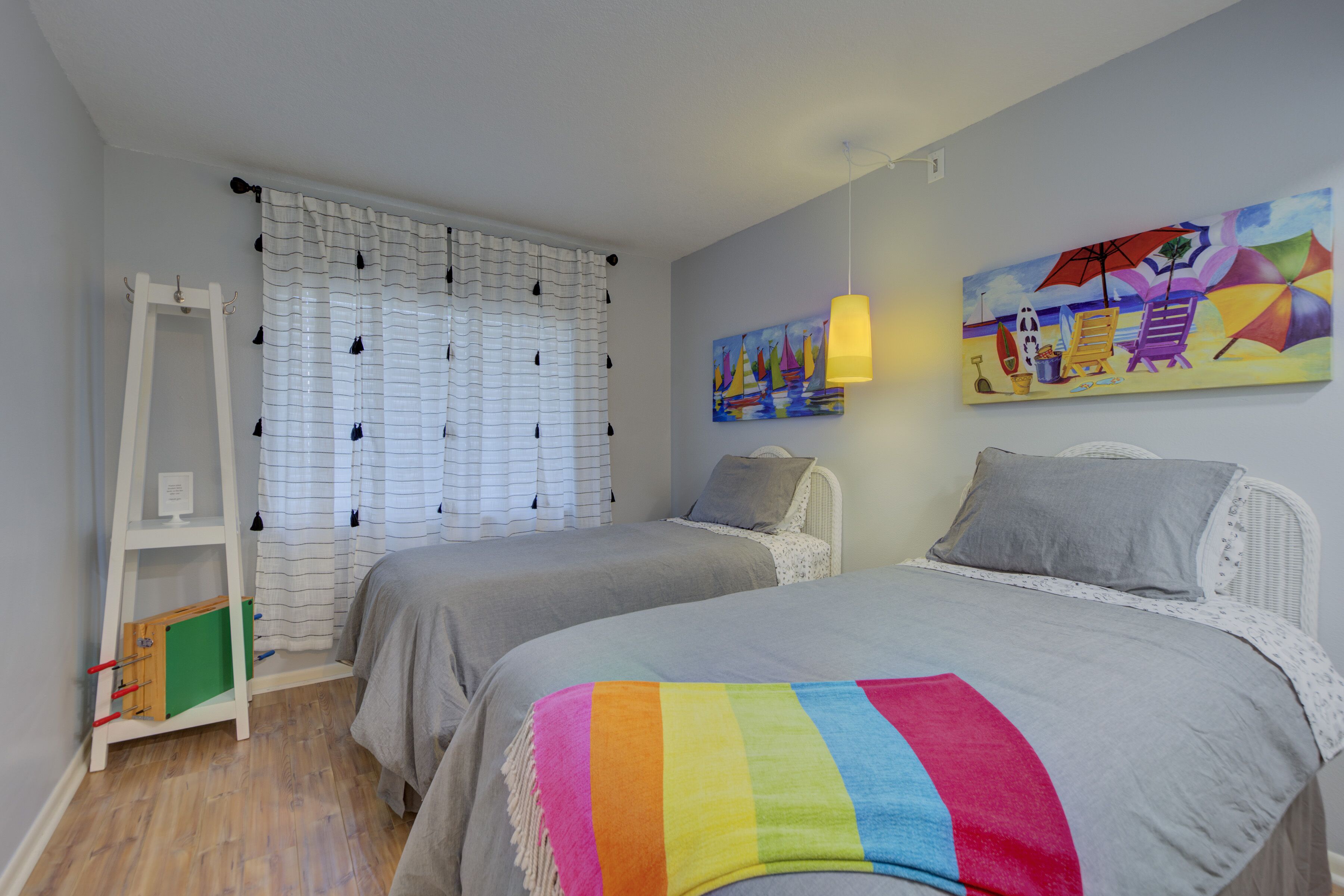 Une chambre avec deux lits, une fenêtre avec des rideaux, un tableau au mur et une étagère.