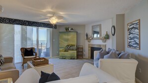 En stue med pejs, loftventilator og stort vindue med udsigt til en balkon.