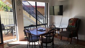 A dining area with a wooden table, four chairs, a television, and a staircase leading outside. - "Strathmore Lodge" - UNIT 1A LOWER LEVEL. (Port Macquarie)
