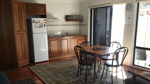 A kitchen with wooden cabinets, a white refrigerator, a dining table with chairs, and a patterned rug. - "Strathmore Lodge" - UNIT 1A LOWER LEVEL. (Port Macquarie)