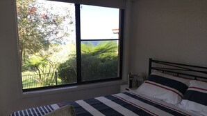 A bedroom with a bed, a window with a view of greenery, and a bedside table with a lamp. - "Strathmore Lodge" - UNIT 1A LOWER LEVEL. (Port Macquarie)