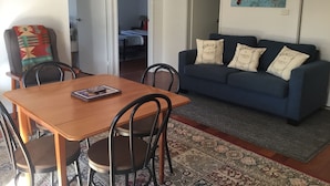 A living room with a blue sofa, patterned rug, and a dining table with chairs. - "Strathmore Lodge" - UNIT 1A LOWER LEVEL. (Port Macquarie)