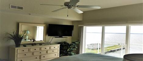 A bedroom with a bed, dresser, TV, and a balcony with a view of the water.