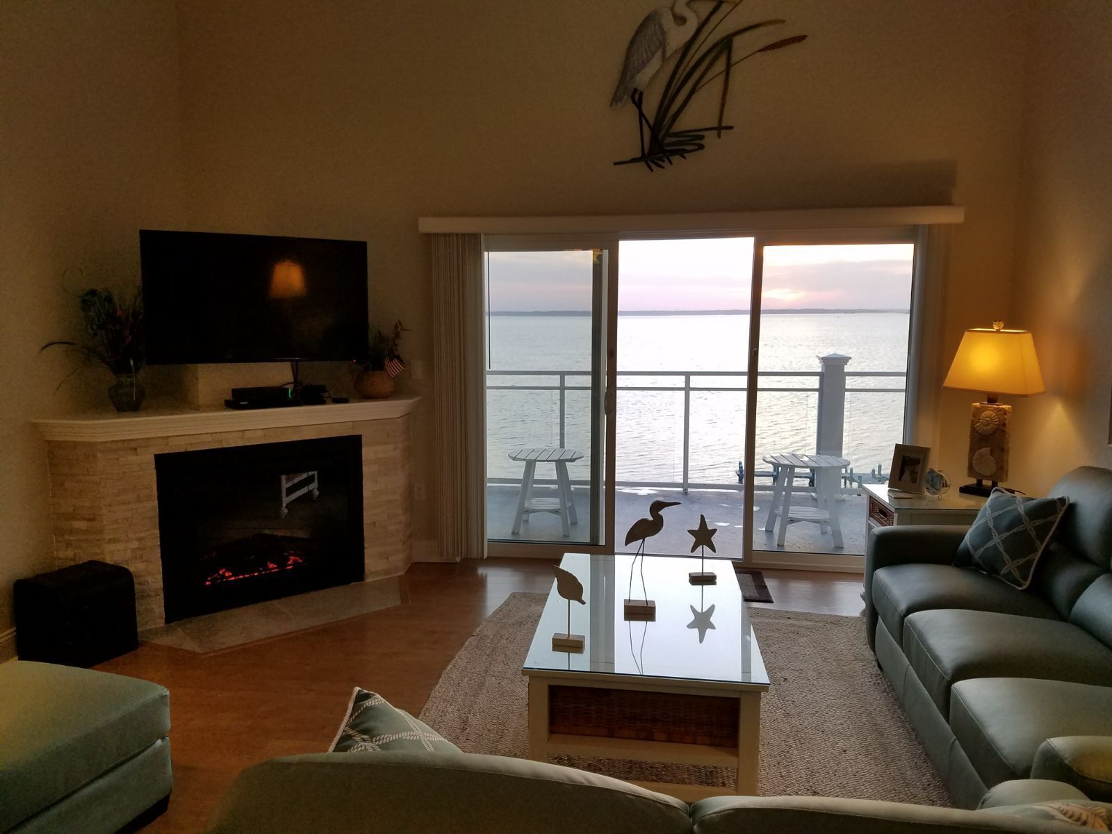 A living room with a fireplace, a television, a sofa, a coffee table, and a view of the sea through large windows.