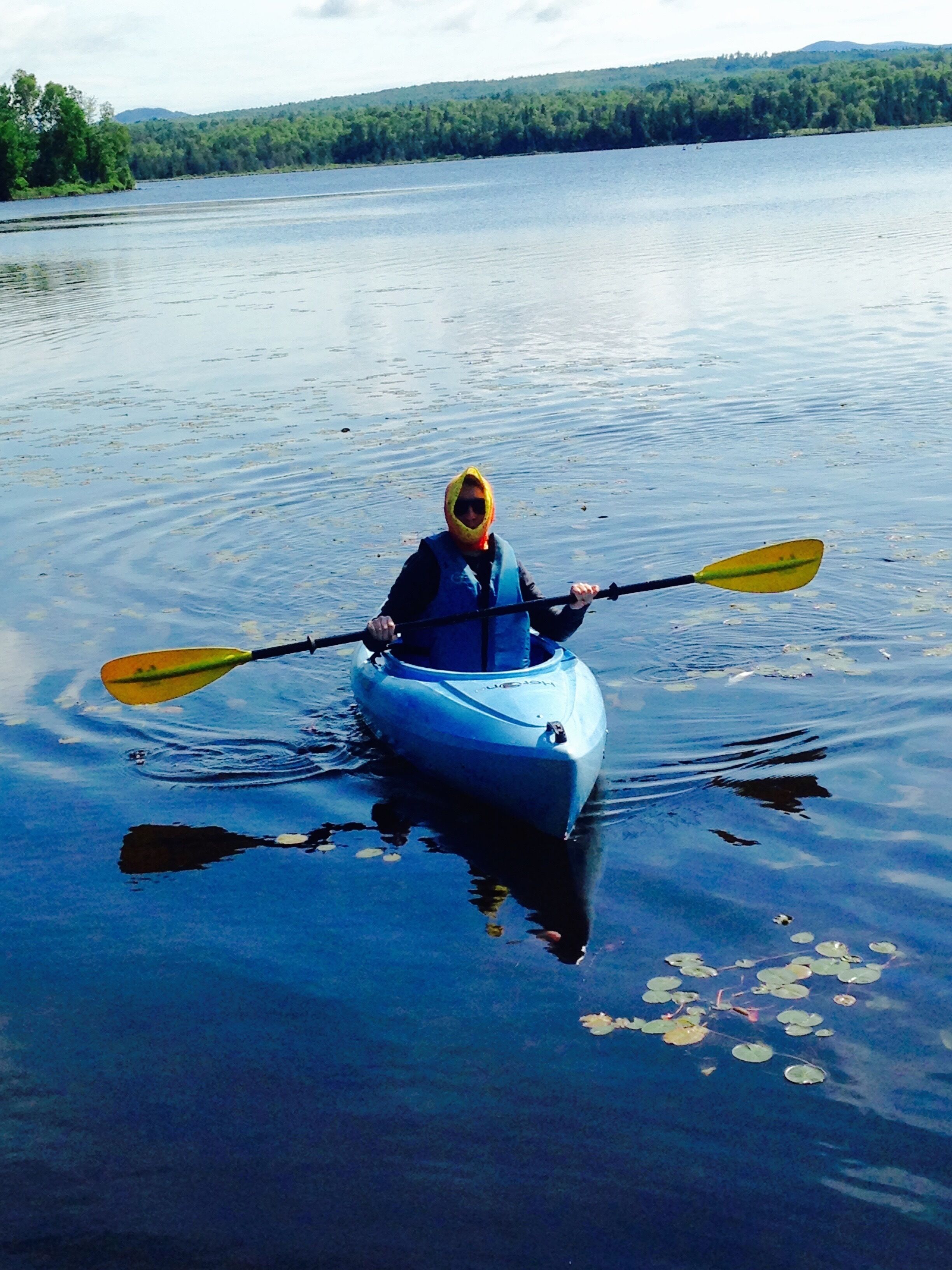 Une personne dans un kayak sur un lac paisible, parsemé de nénuphars.