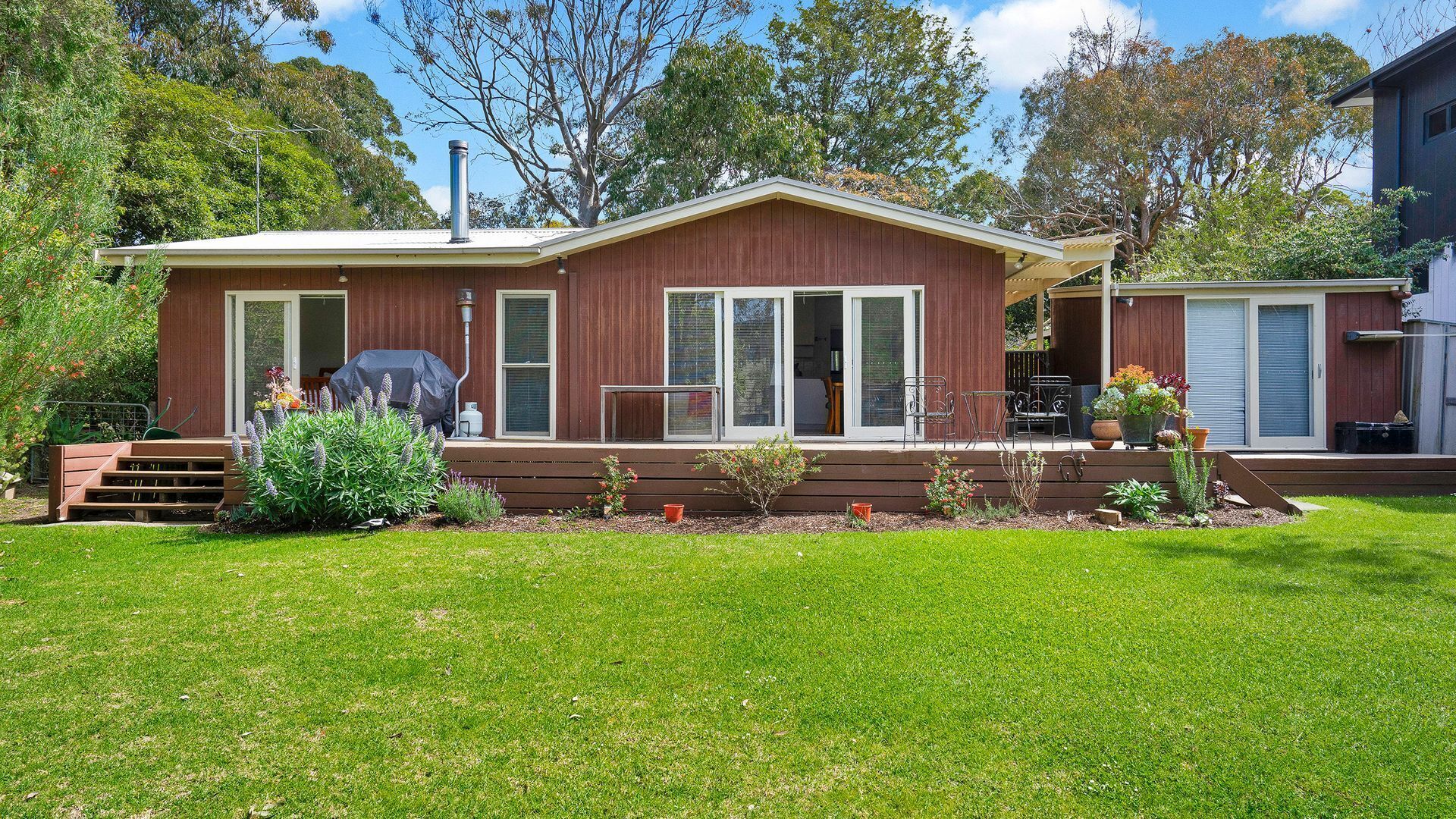 A two-story house with a front porch, a barbecue grill, and a small garden.