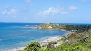 Un paysage côtier avec une plage, une eau d’un bleu limpide et une colline parsemée de constructions.