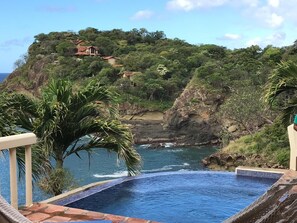 Une piscine avec vue sur l’océan et une colline parsemée de bâtiments.