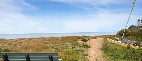 A bench and a canoe on a sandy path leading to a beach.