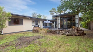 A modern two-story house with a large glass door entrance, a patio with outdoor furniture, and a well-maintained lawn. - Tranquil Oasis - Pet friendly (BALNARRING BEACH)