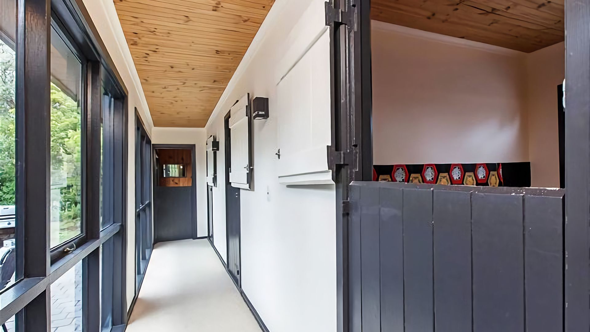 A hallway with large windows, a wooden ceiling, and a tiled wall with a clock.