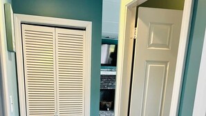 Un couloir avec une porte blanche et un placard aux portes à persiennes.