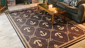 Un salon doté d’une cheminée en briques, d’un canapé agrémenté de coussins à motifs, d’une table basse et d’un tapis orné de motifs d’ancres.