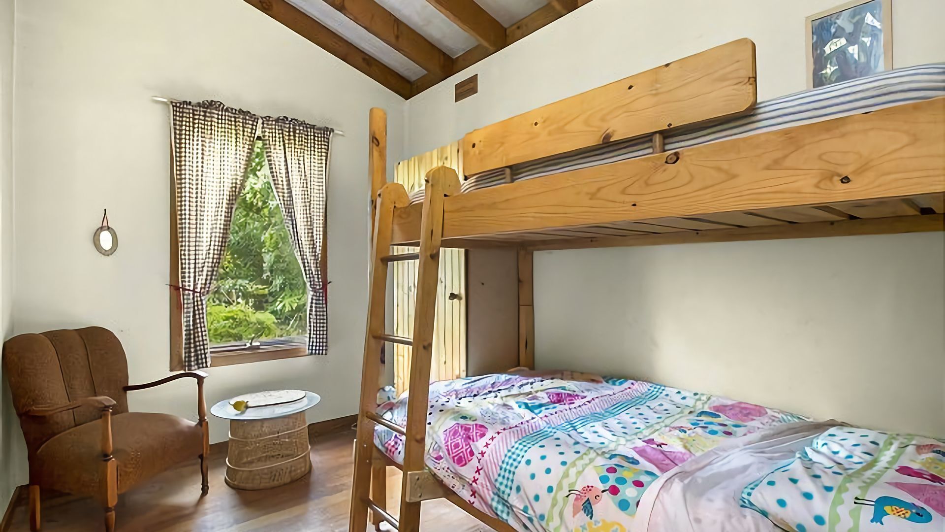 A bunk bed room with a window, a chair, and a small round table.