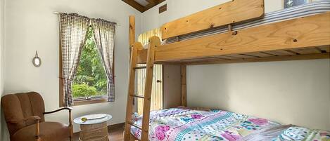 A bunk bed room with a window, a chair, and a small round table.