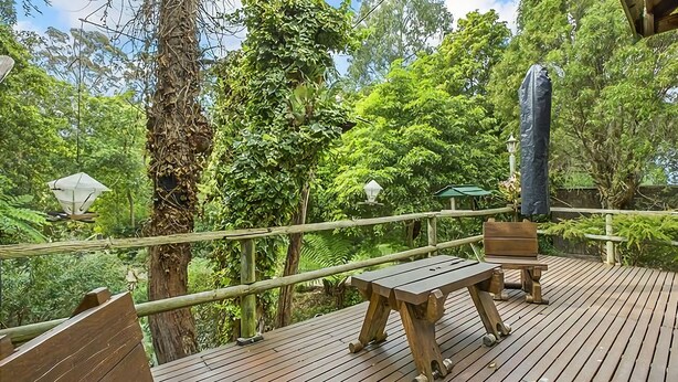 Een houten terras met een tafel en stoelen, omringd door weelderige begroeiing en bomen.