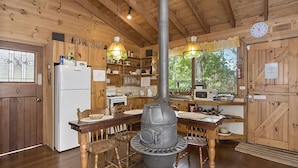 Een rustieke keuken met houten wanden, een houten kachel in het midden en een eethoek met een houten tafel en stoelen.