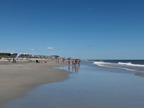 Une plage avec un ciel dégagé, un rivage sablonneux et quelques bâtiments en arrière-plan.