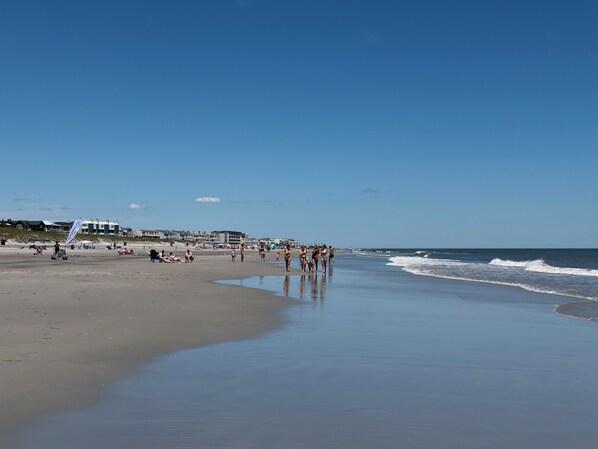 A beach with a clear sky, a sandy shore, and a few buildings in the background.