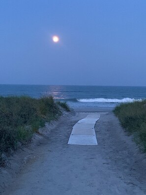 En sti af sand der fører ned til havet, med en måne på himlen.