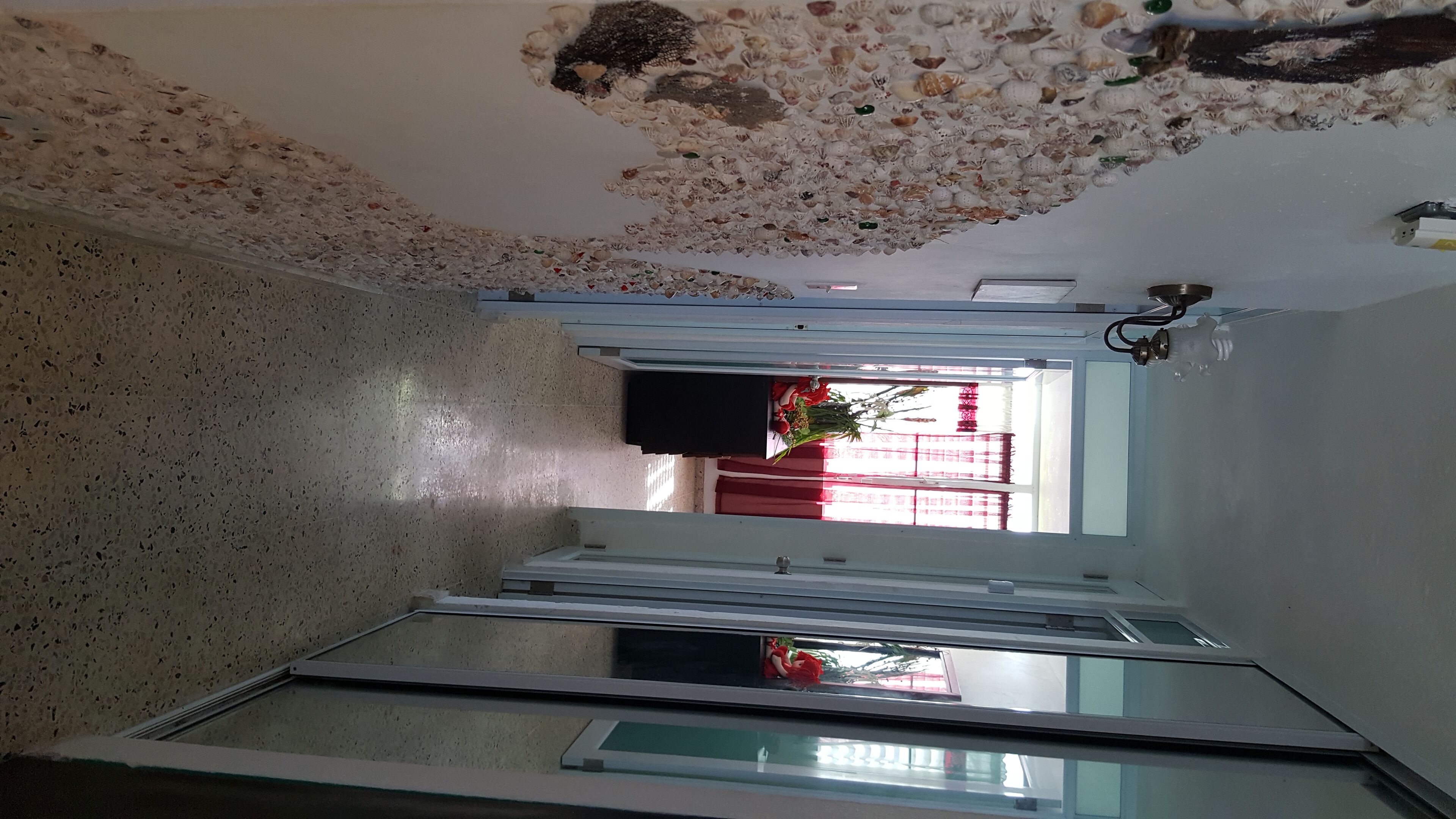A room with a speckled floor, a glass partition, and a ceiling decorated with seashells.