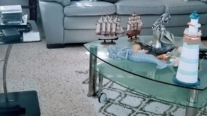 A living room with a grey sofa, a glass coffee table with decorative items, a painting on the wall, and a vase with flowers.