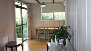 Habitació amb taula de dinar de fusta, dues cadires, una planta en test i una finestra amb cortines.