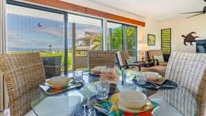 A dining area with wicker furniture, a glass table, and a view of a house and palm trees.