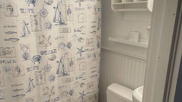 Une salle de bain avec un rideau de douche à motifs nautiques, des toilettes blanches et une étagère contenant des articles de toilette.