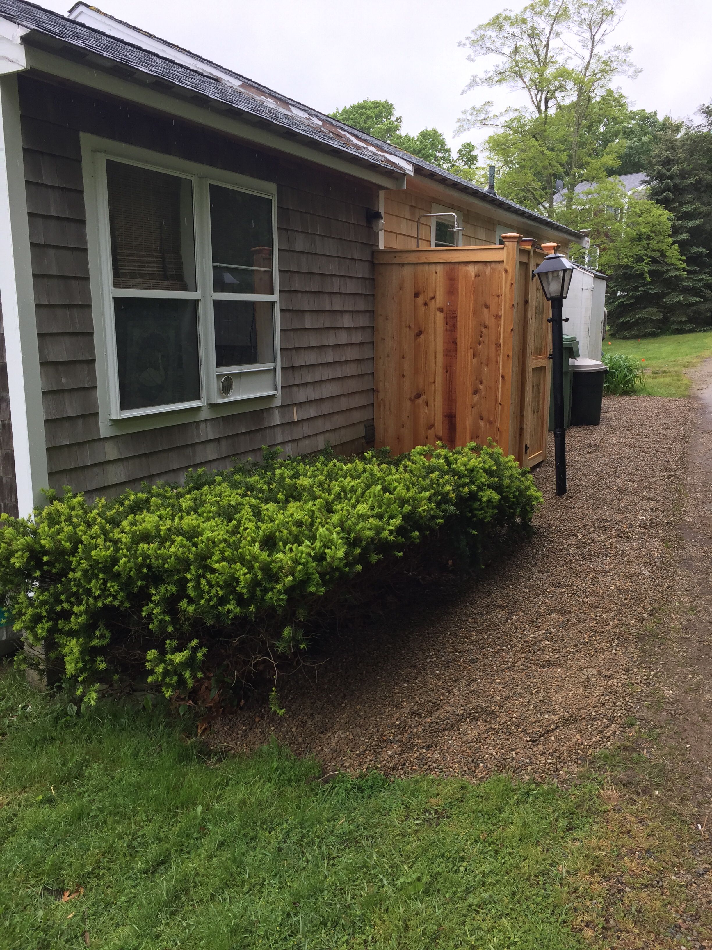 A house with a wooden fence, a gravel driveway, and a green bush in front.