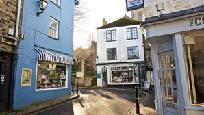Vista de calle con un edificio azul a la izquierda, un edificio blanco con un letrero que dice "The Cornish Bakery", y una tienda con un letrero que dice "Enjoy".